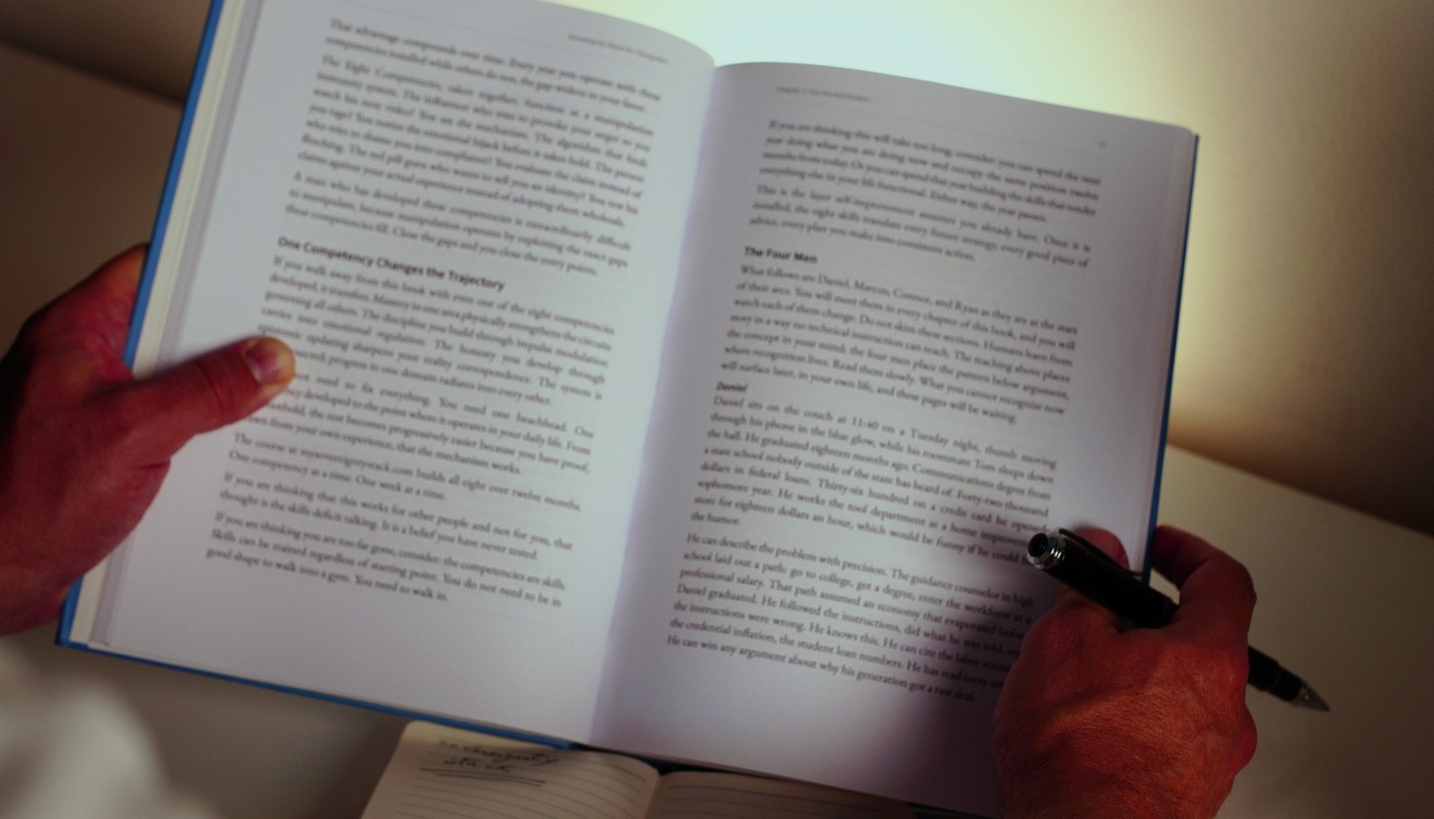 A pair of hands holding the open hardcover, with a pen resting on the page.